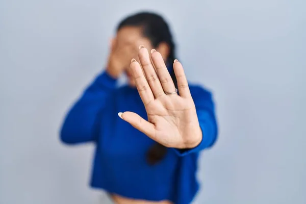 Young hispanic woman standing over isolated background covering eyes with hands and doing stop gesture with sad and fear expression. embarrassed and negative concept.