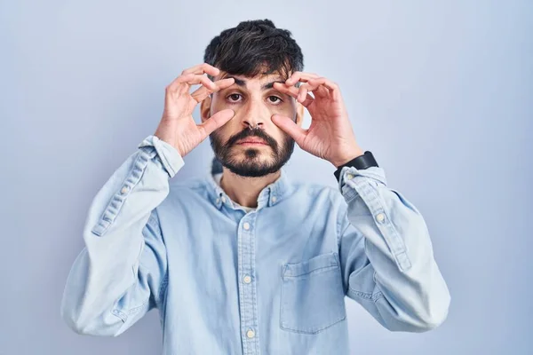 Jovem Hispânico Com Barba Sobre Fundo Azul Tentando Abrir Olhos — Fotografia de Stock