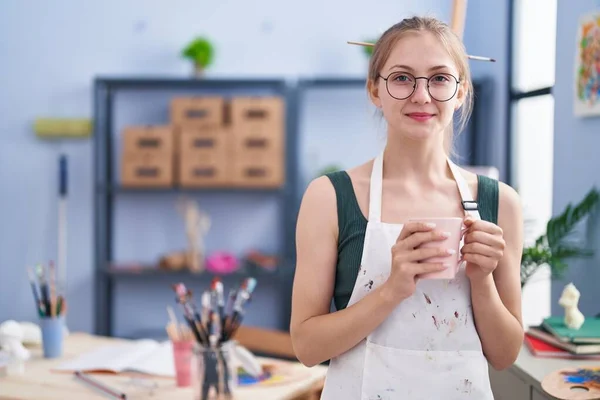 年轻的高加索女艺术家站在艺术工作室喝咖啡 — 图库照片