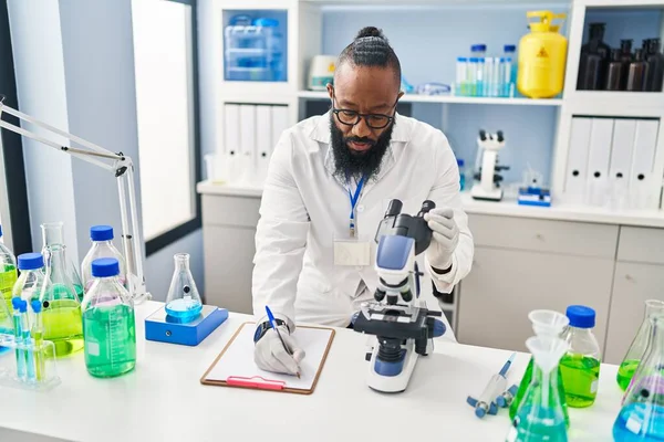 研究室で顕微鏡を使って科学者の制服を着た若いアフリカ系アメリカ人 — ストック写真
