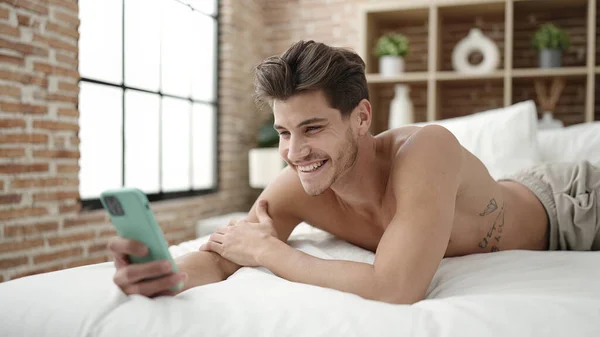 年轻的他的惊慌失措的男人靠智能手机自作主张躺在卧室的床上 — 图库照片