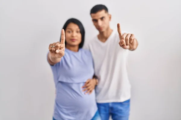 赤ん坊を期待している若いヒスパニック系のカップルは 背景に指を指していると怒りの表情 ジェスチャーを示しません — ストック写真