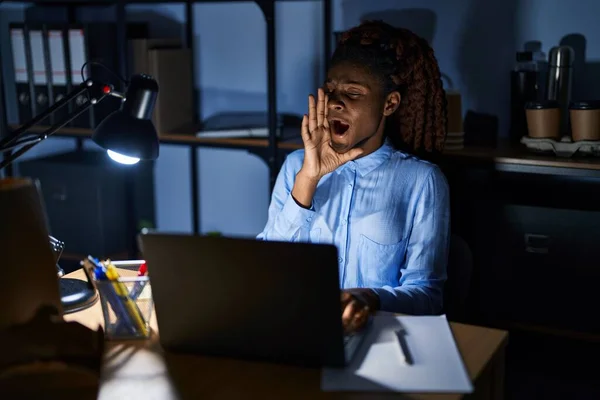 African woman working at the office at night shouting and screaming loud to side with hand on mouth. communication concept.