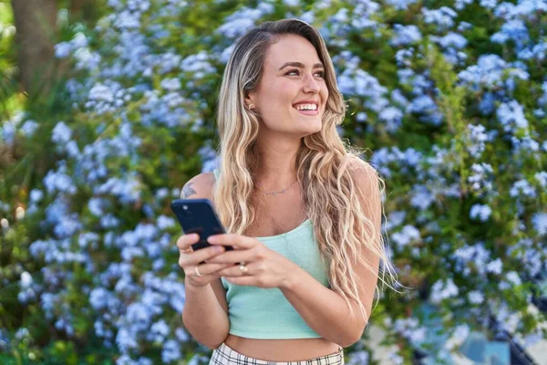 年轻的金发女人在公园用智能手机充满自信地微笑 — 图库照片