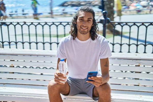 Ung Latinamerikan Man Med Smartphone Håller Flaska Vatten Vid Havet — Stockfoto