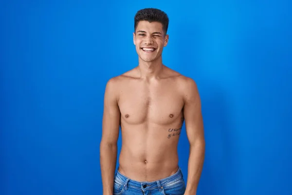 Joven Hombre Hispano Pie Sin Camisa Sobre Fondo Azul Guiño —  Fotos de Stock