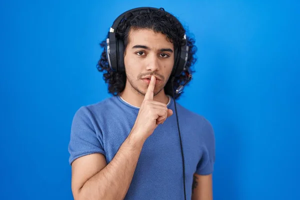 西班牙裔男人 用耳机听音乐 要求安静 手指放在嘴唇上 沉默和秘密概念 — 图库照片
