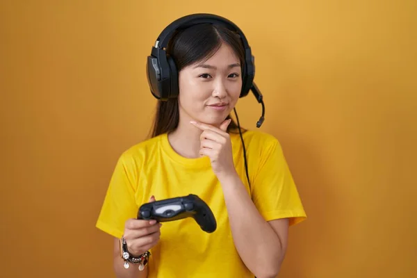 中国年轻女子玩电子游戏时 抱着控制器 满脸自信地看着摄像机 双臂交叉 双手托着下巴 积极地思考 — 图库照片