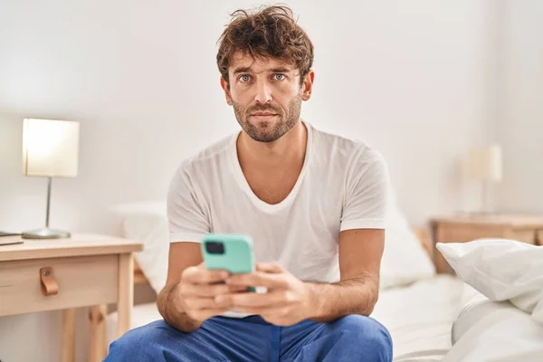 Genç Adam Yatakta Otururken Ciddi Bir Ifadeyle Akıllı Telefon Kullanıyor — Stok fotoğraf