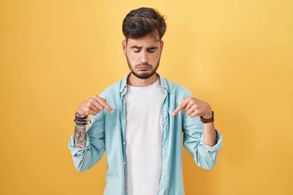 Young Hispanic Man Tattoos Standing Yellow Background Pointing Looking Sad — Stock Fotó