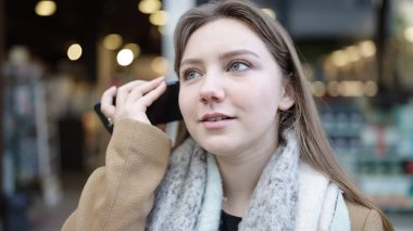 Young blonde woman smiling confident listening audio message by the smartphone at street