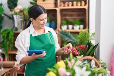 Young beautiful hispanic woman florist smiling confident using touchpad at flower shop