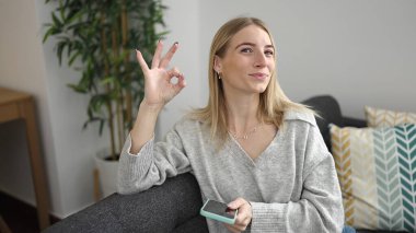 Akıllı telefon kullanan genç sarışın kadın evde imza atıyor.