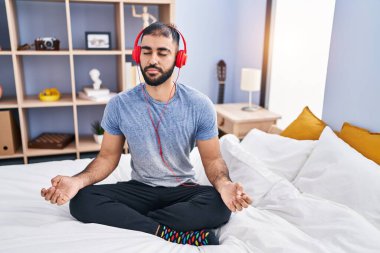 Young hispanic man doing yoga exercise sitting on bed at bedroom
