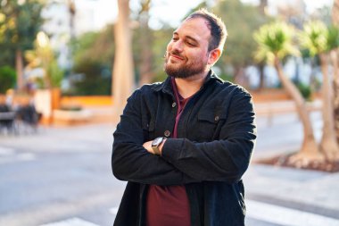 Young hispanic man smiling confident standing with arms crossed gesture at street
