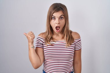 İzole edilmiş arka planda dikilen genç İspanyol kadın elleri yana doğru işaret ederek şaşırdı, ağzı açık şaşkın bir ifadeyle.. 