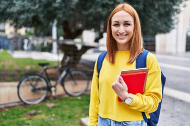 Young caucasian woman student smiling confident holding books at park