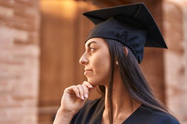 Young hispanic woman wearing graduated uniform standing with relaxed expression at university