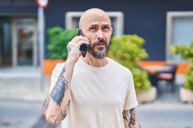 Genç kel adam akıllı telefonda konuşuyor. Sokakta ciddi bir ifadeyle.