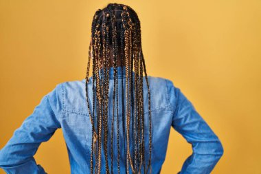 Saçları sarı arka planda dikilmiş, kolları vücudunda olan Afrikalı Amerikalı kadın. 