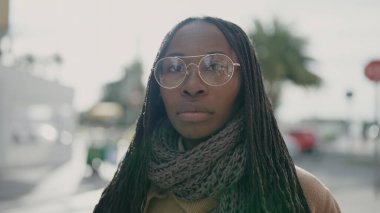 African woman standing with serious expression wearing glasses at street