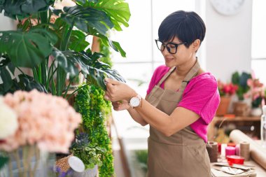 Middle age chinese woman florist smiling confident touching plant at flower shop
