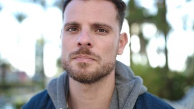 Parkta yüzü ciddi bir ifadeyle duran beyaz bir genç.