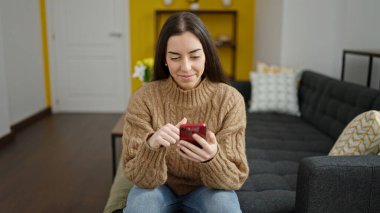 Evdeki kanepede oturan akıllı telefon kullanan genç, güzel İspanyol kadın.