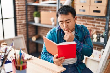Young chinese man artist reading book at art studio