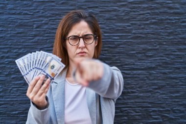 Elinde dolarlarla kamerayı işaret eden esmer bir kadın ve sen, kendine güvenen ciddi görünüyorsun. 