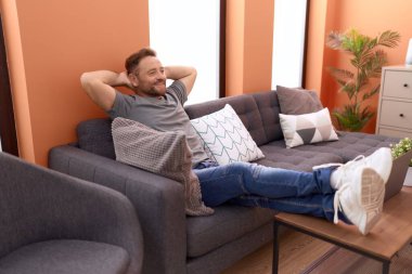 Middle age man relaxed with hands on head sitting on sofa at home