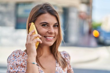 Gülümseyen genç bir kadın caddedeki akıllı telefondan konuşuyor.