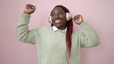 Saçları örgülü, gülümseyen ve dans eden, kulaklık takan, izole pembe arka planı olan Afrikalı bir kadın.