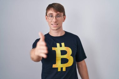 Bitcoin tişörtü giyen beyaz sarışın adam selamlama ve hoş geldin demek için dostça tokalaşıyor. başarılı iş. 