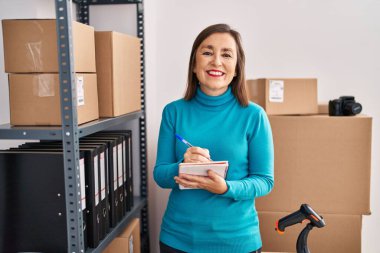 Orta yaşlı kadın ecommerce iş işçisi ofisteki deftere yazıyor.