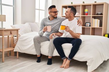 Two men couple drinking cup of coffee hugging each other at bedroom