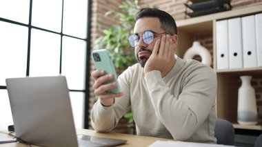 Genç İspanyol iş adamı ofiste akıllı telefon kullanıyor.