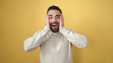 İzole edilmiş sarı arka planda sürpriz bir ifadeyle duran İspanyol genç adam.
