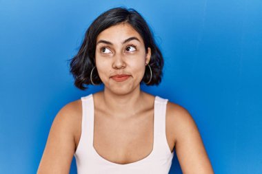 Mavi arka planda duran genç İspanyol kadın gülümsüyor, yan tarafa bakıyor ve düşünüyor.. 