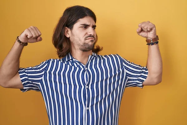 Hispanic Man Long Hair Standing Yellow Background Showing Arms Muscles — Stock Photo, Image
