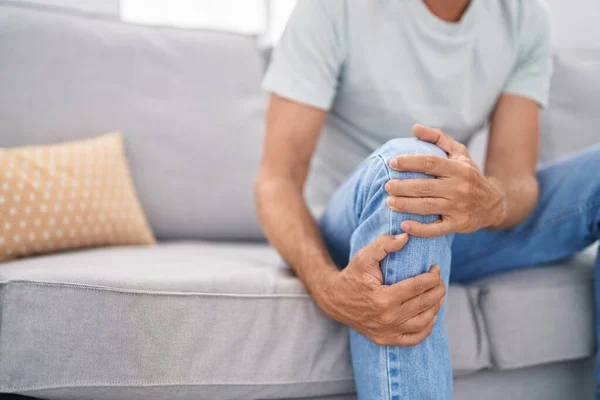 stock image Young man suffering for knee injury sitting on sofa at home