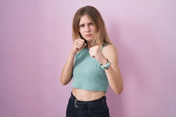 ブロンド原因アジアの女性スタンディングピンクの背景パンチング拳で戦うために 積極的かつ怒っている攻撃 脅威と暴力 — ストック写真