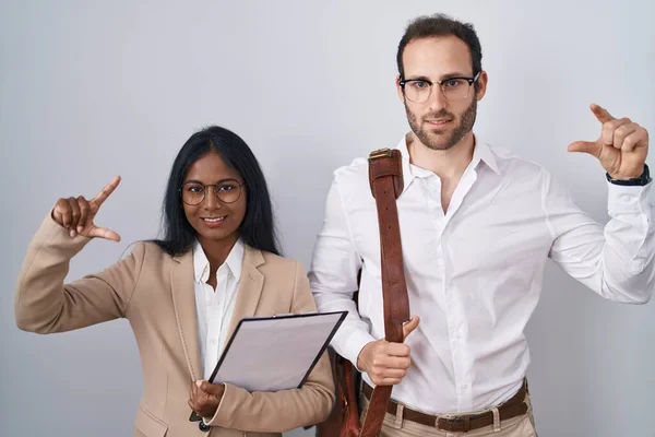 stock image Interracial business couple wearing glasses smiling and confident gesturing with hand doing small size sign with fingers looking and the camera. measure concept. 