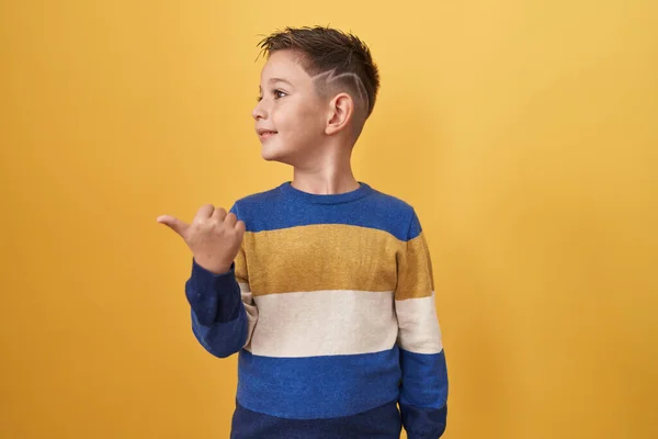 小さなヒスパニック系の男の子立っている上に黄色の背景指差す親指へ側笑顔で幸せとともにオープン口 — ストック写真