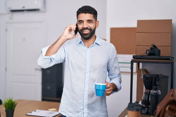 若いアラブ人のビジネスマンがオフィスでスマートフォンのコーヒーを飲む話 — ストック写真