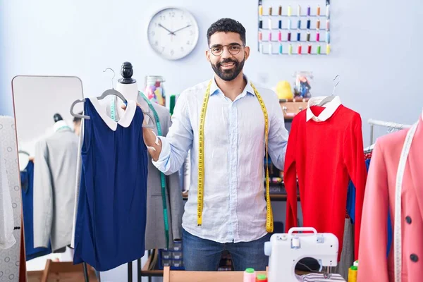 年轻的阿拉伯男子裁缝笑着自信地在裁缝店里拿着T恤衫 — 图库照片