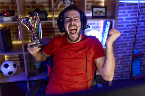 Νεαρός Ισπανόφωνος Παίζει Βιντεοπαιχνίδια Κρατώντας Τρόπαιο Φωνάζοντας Περήφανος Γιορτάζοντας Νίκη — Φωτογραφία Αρχείου