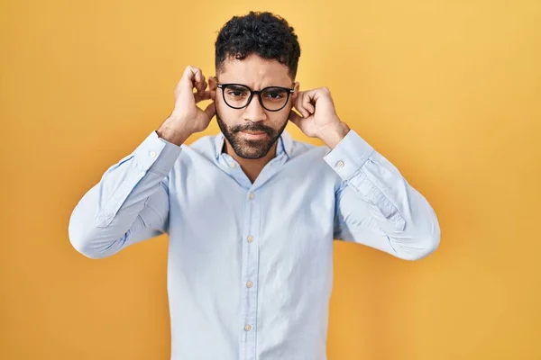 Hispanic Man Beard Standing Yellow Background Covering Ears Fingers Annoyed — Fotografia de Stock