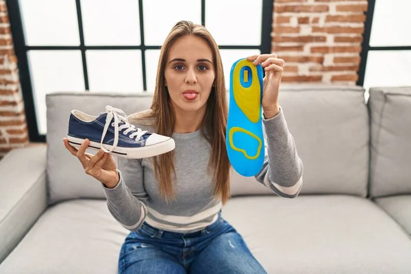 Young woman holding shoe insole sticking tongue out happy with funny expression.