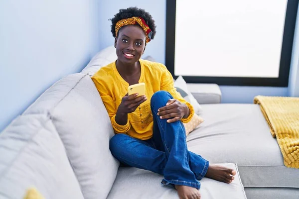 年轻的非洲裔美国女人坐在家里的沙发上用智能手机 — 图库照片